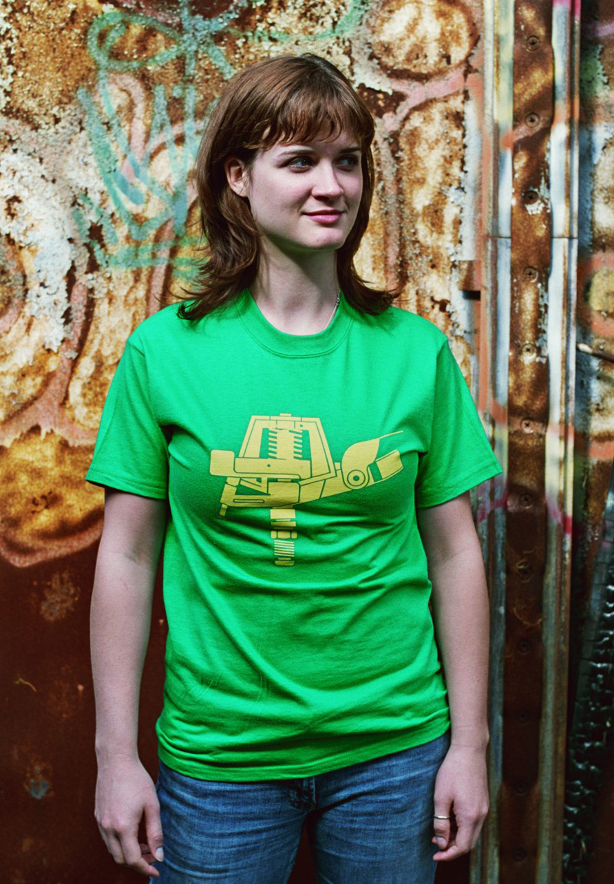 Photograph of a woman modeling a green t-shirt with a yellow geometric illustration of a sprinkler head for lawns.