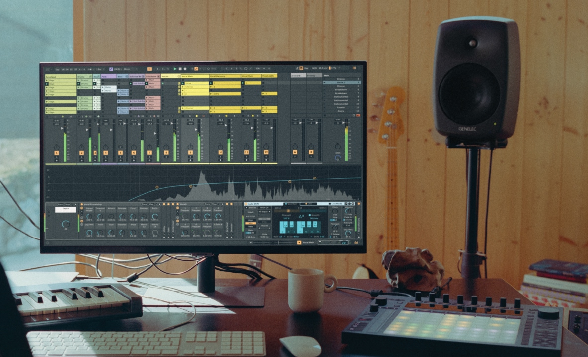 A photograph of a home music studio workspace including a computer display and musical keyboard.